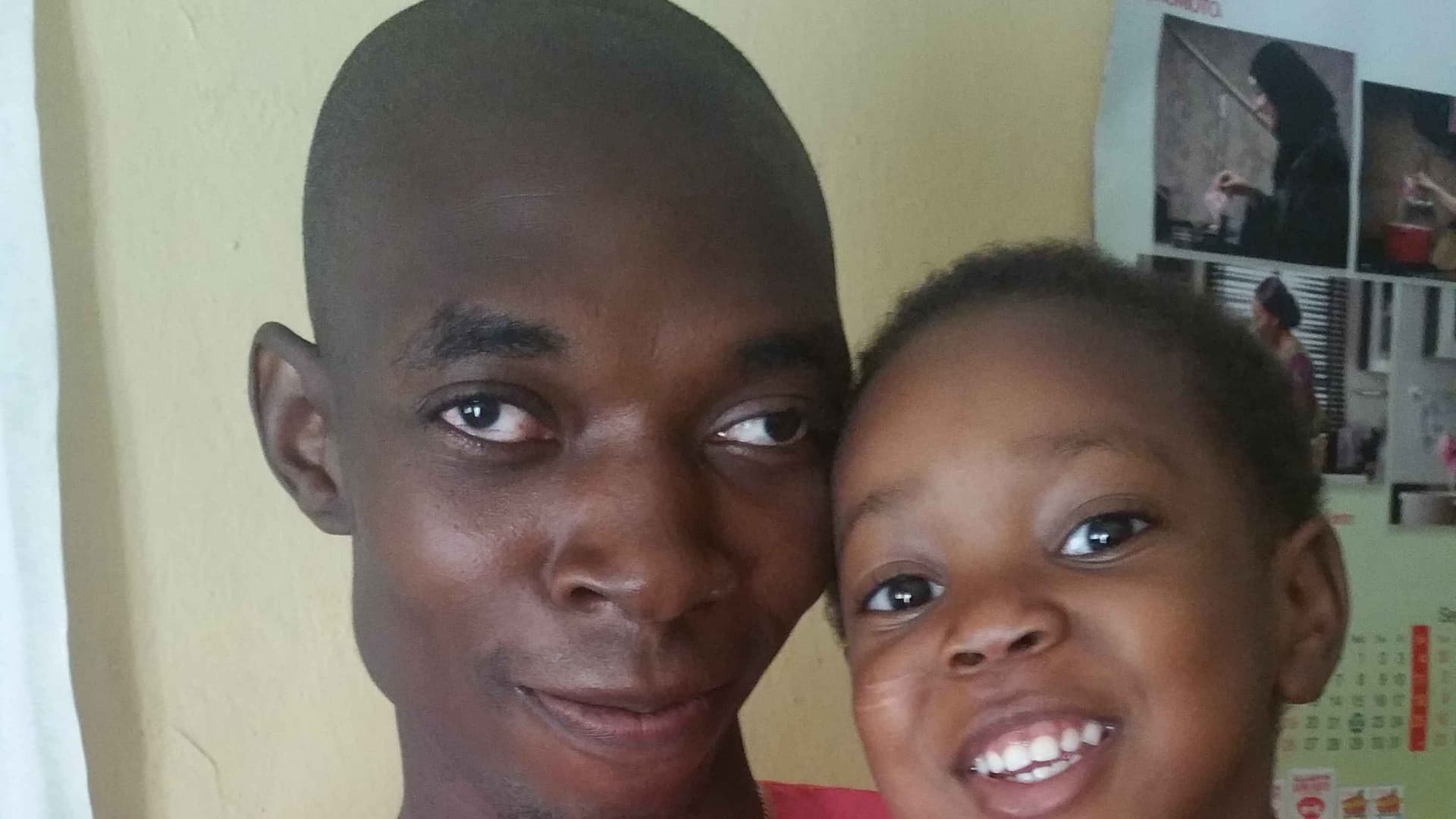 A young autistic man called dogo carrying his niece who is about 5 years old, he is dark while she is fair they are both wearing pink colored Ankara.