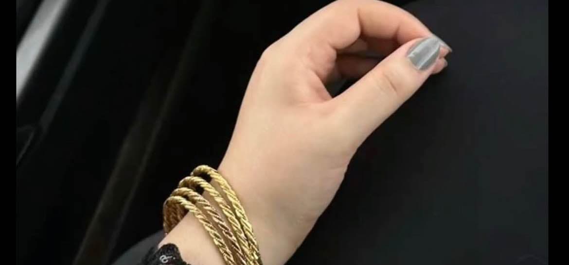 A close-up photograph of a woman’s hand wearing several golden bangles, gently raised against a dark background.
